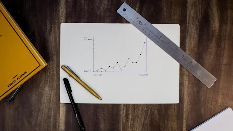 A hand-drawn upward trend line on graph paper beside a ruler and pen.