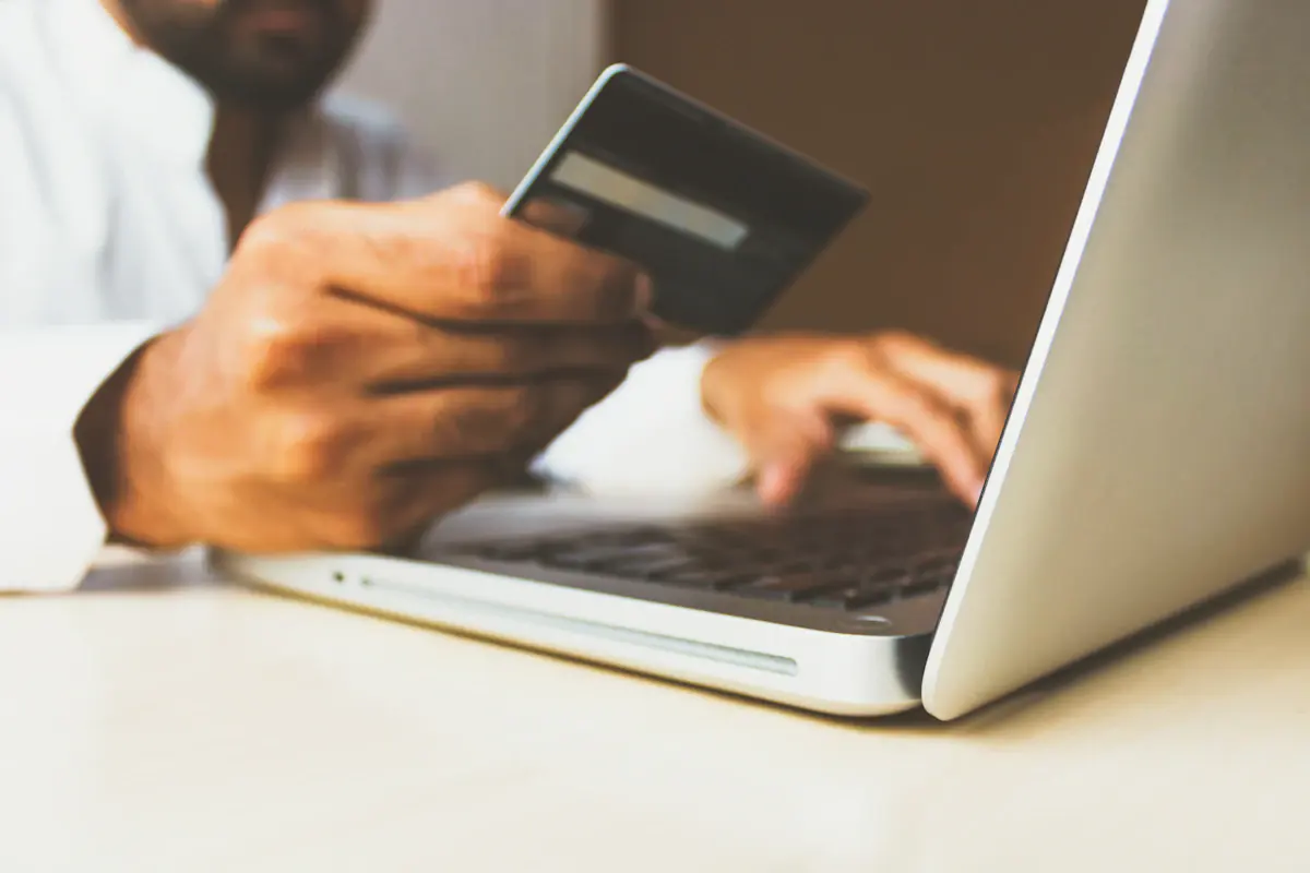 A person holding a bank card while typing on a laptop, funding an account.